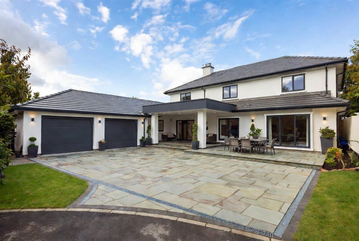 A large modern home with an expansive sandstone-paved patio and driveway in a landscaped UK garden